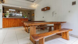 A wooden bench and table in a room with a tiled floor and a kitchen area in the background. - Hotel O Canggu Near Echo Beach Formerly Saren Guesthouse (Kerobokan)
