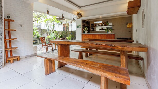 A spacious indoor area with a wooden bench and a small table, a brick wall, and a view of a garden with trees and a pond. - Hotel O Canggu Near Echo Beach Formerly Saren Guesthouse (Kerobokan)