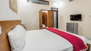 A hotel room with a large bed, a television, a refrigerator, and a wooden wall panel. - Hotel O Canggu Near Echo Beach Formerly Saren Guesthouse (Kerobokan)