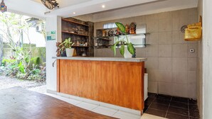A reception area with a wooden counter, glass shelves, and potted plants. - Hotel O Canggu Near Echo Beach Formerly Saren Guesthouse (Kerobokan)