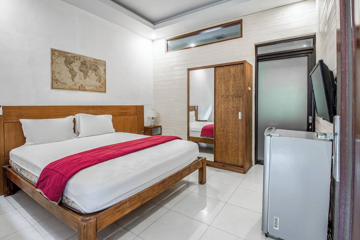 Ein Hotelzimmer mit einem hölzernen Bett, einem kleinen Schreibtisch, einem Spiegel, einem Kleiderschrank und einem Fernseher.