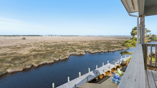 Terraza de madera con vista a un río y a una costa lejana.