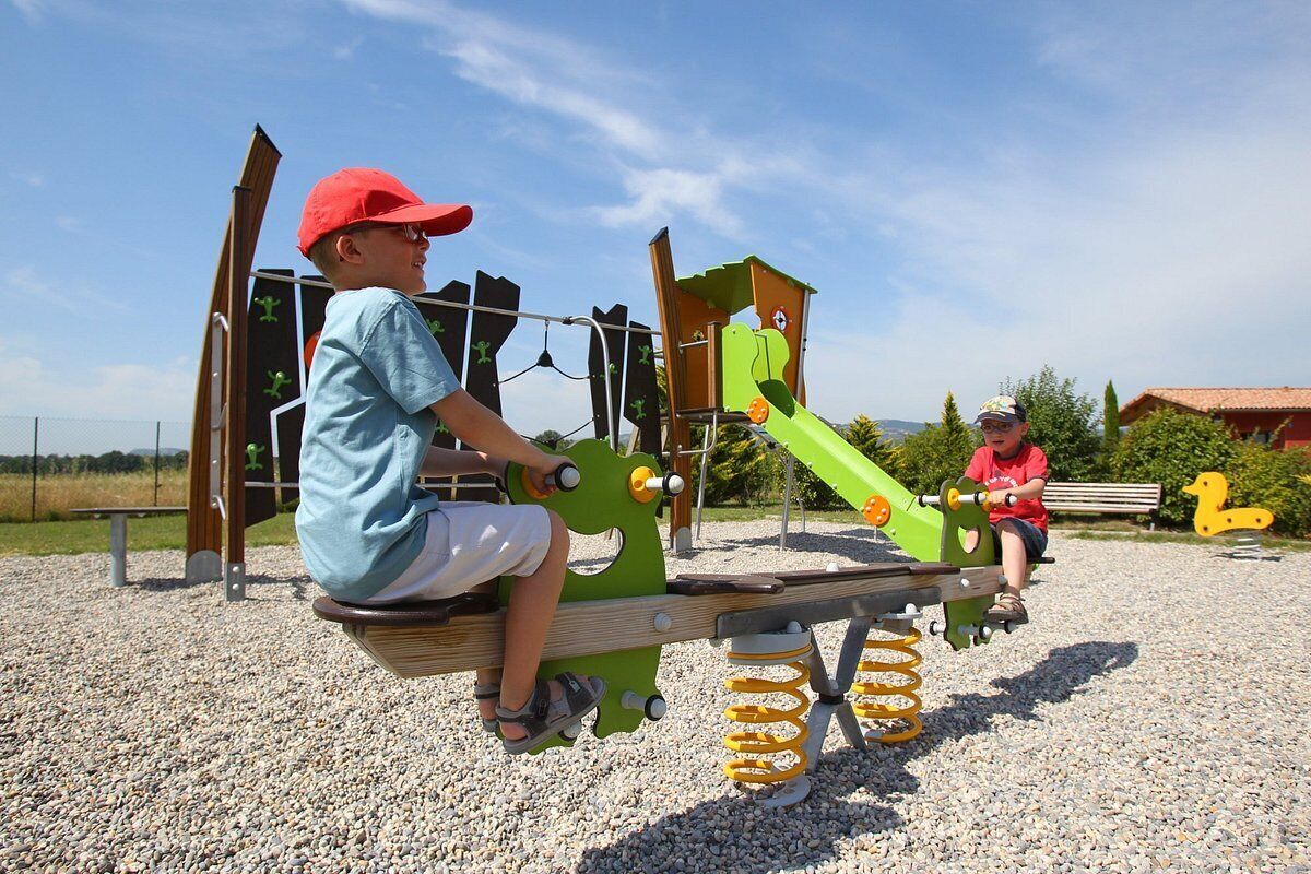 Two children playing on a playground with a seesaw and a slide.