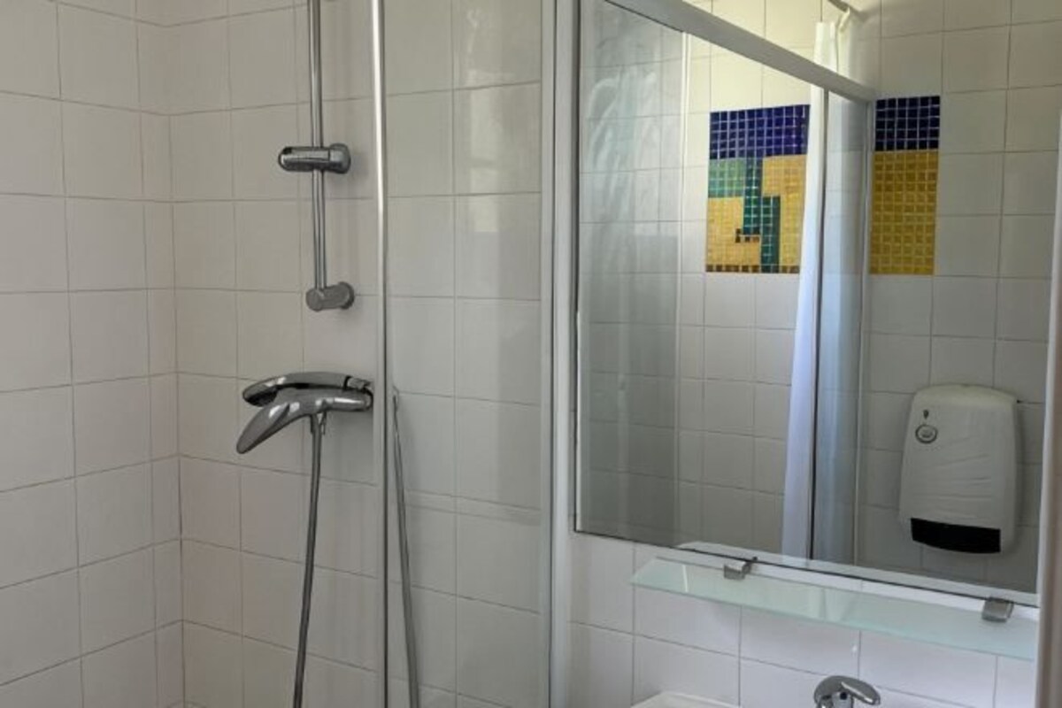 A bathroom with a glass shower enclosure, a mirror, and a soap dispenser.