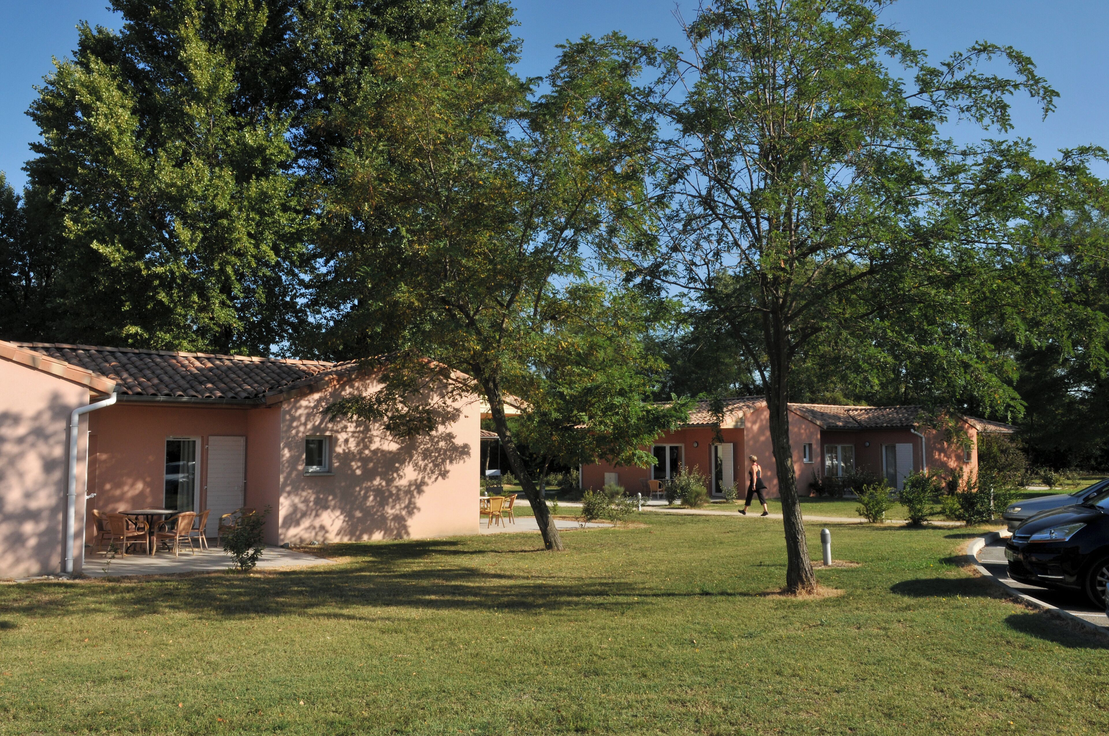 Una zona residenziale con due case basse, un prato e un'auto parcheggiata.