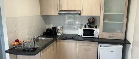A compact kitchen with wooden cabinets, a microwave, a coffee maker, and a small refrigerator.