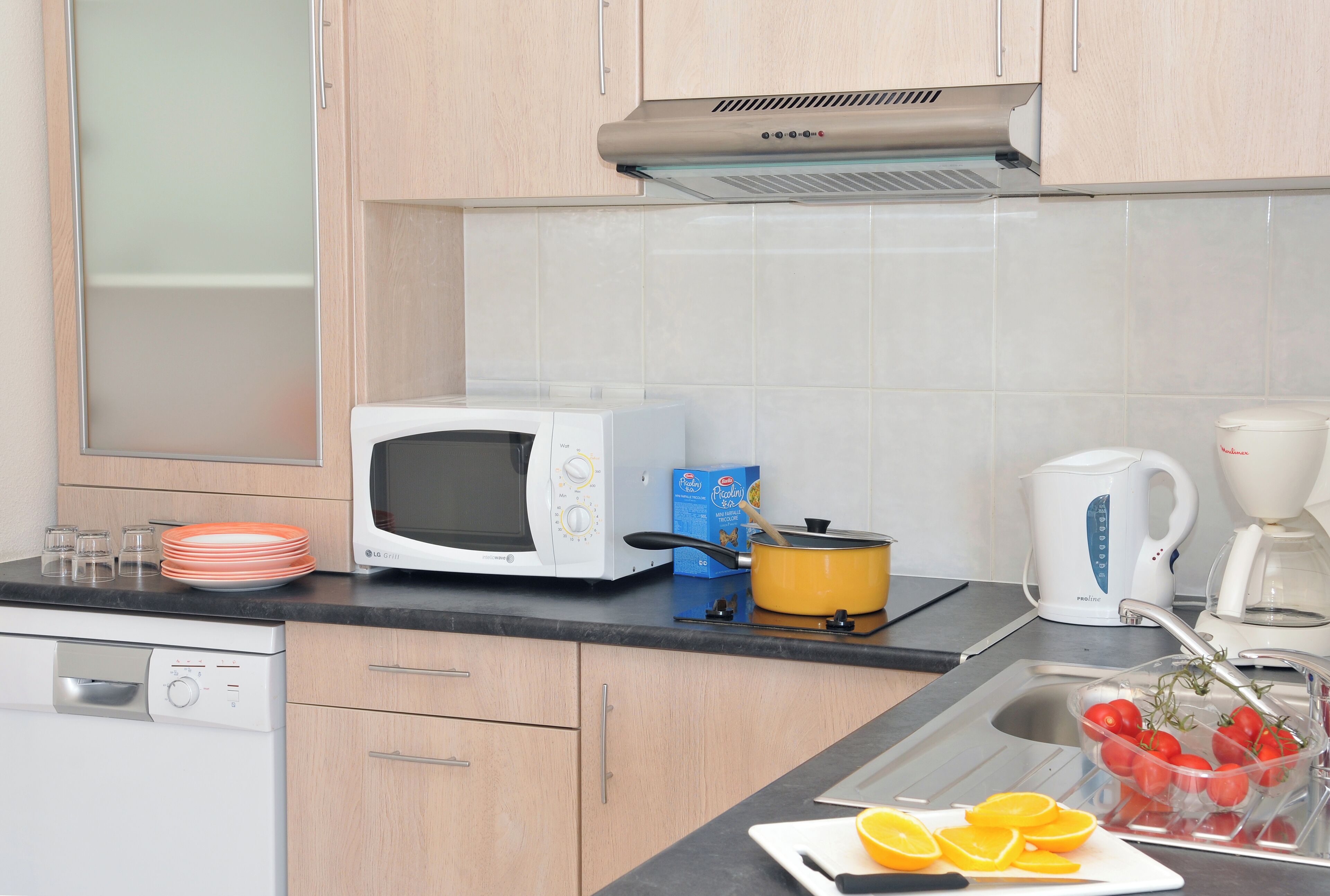 A kitchen with a microwave, a coffee maker, a kettle, and a sink with a dish rack.