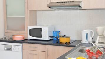 A kitchen with a microwave, a coffee maker, a kettle, and a sink with a dish rack.