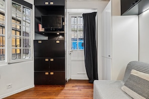Un couloir étroit avec un meuble de rangement noir, une porte blanche et une fenêtre donnant sur une piscine bleue.