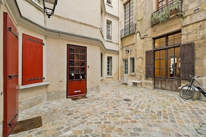 A narrow cobblestone alley with a red door, a bicycle, and a bench.