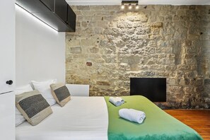 Une chambre avec un mur en pierre, un lit recouvert d’une couverture verte et une tête de lit noire.