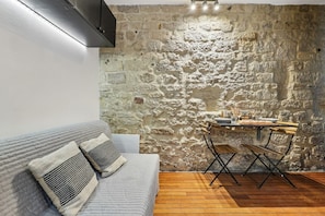 Une pièce avec un mur en pierre, une table à manger en bois avec des chaises, un canapé gris avec des coussins et un plancher en bois.