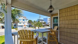 A porch with two Adirondack chairs, a table, and a hanging lantern. - 🌴 Surf Haus: Fenced Yard | 1 Block to the Beach | Screened-In Porch 🌴 (Carolina Beach)
