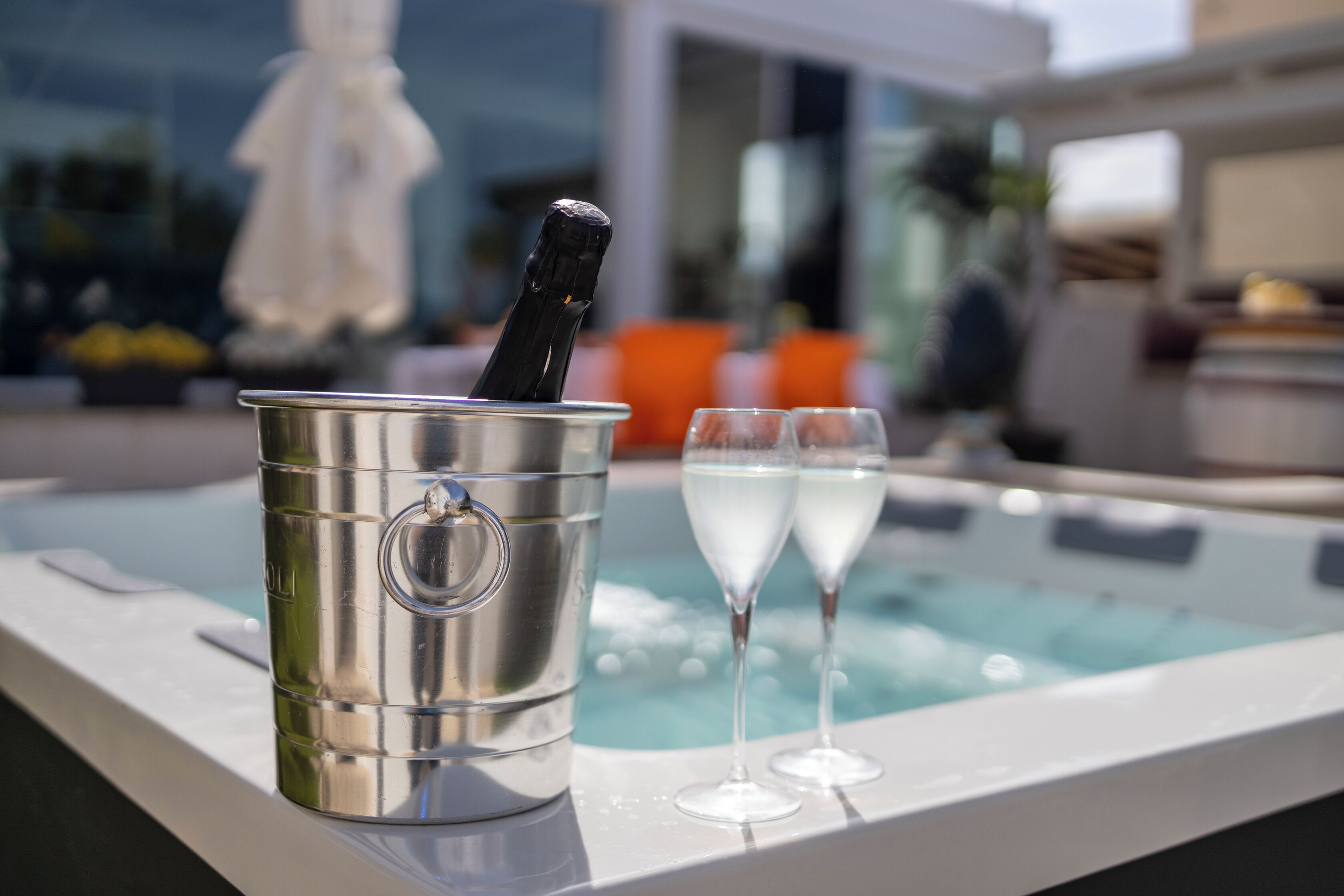 Ein Whirlpool mit Champagnergläsern, einem Metallkübel und einem weißen Sonnenschirm im Hintergrund.