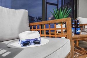 A wicker hat and sunglasses on a gray sofa, a wooden chair, and a table with bottles and glasses.