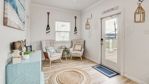 A room with a wooden floor, two armchairs, a small table, a decorative cabinet, a door labeled "SEASHORE", and a view of a wooden deck outside. - Serene Surfside Beach Retreat w/ Ocean Views! (Freeport)