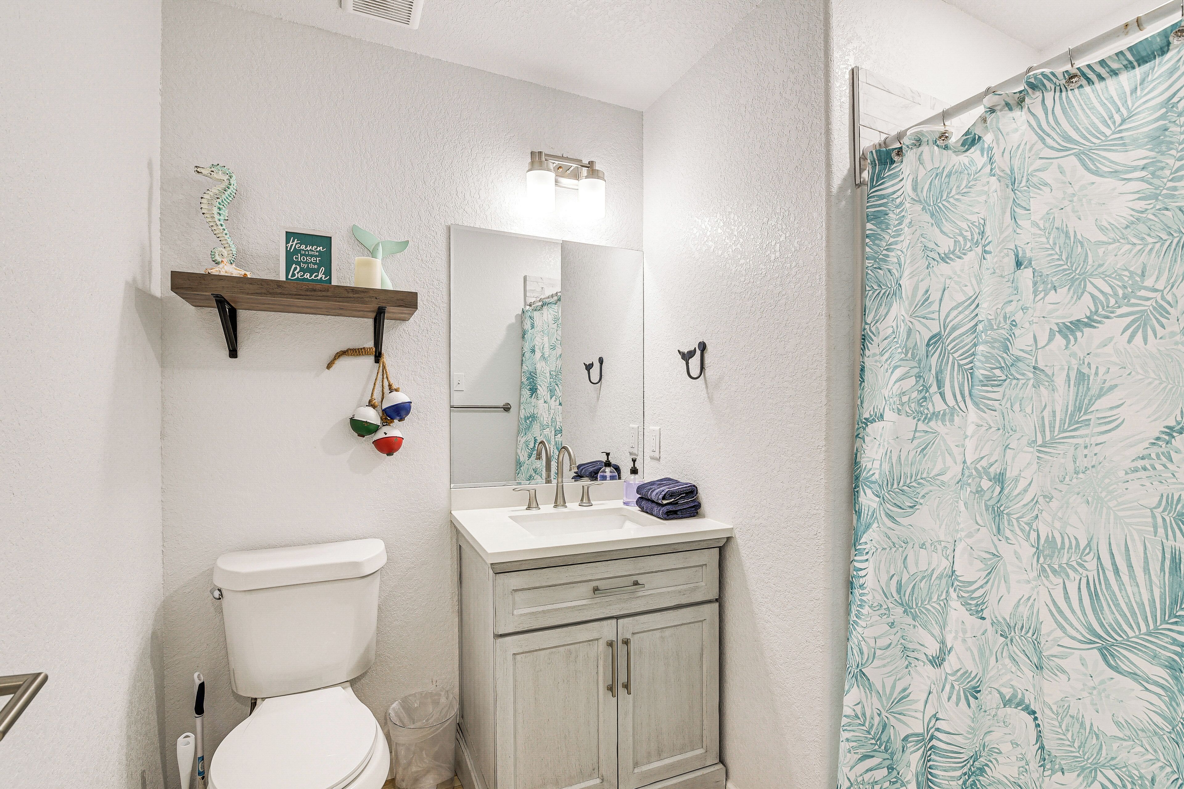A bathroom with a toilet, sink, and mirror. There is a shower curtain with a leaf pattern.