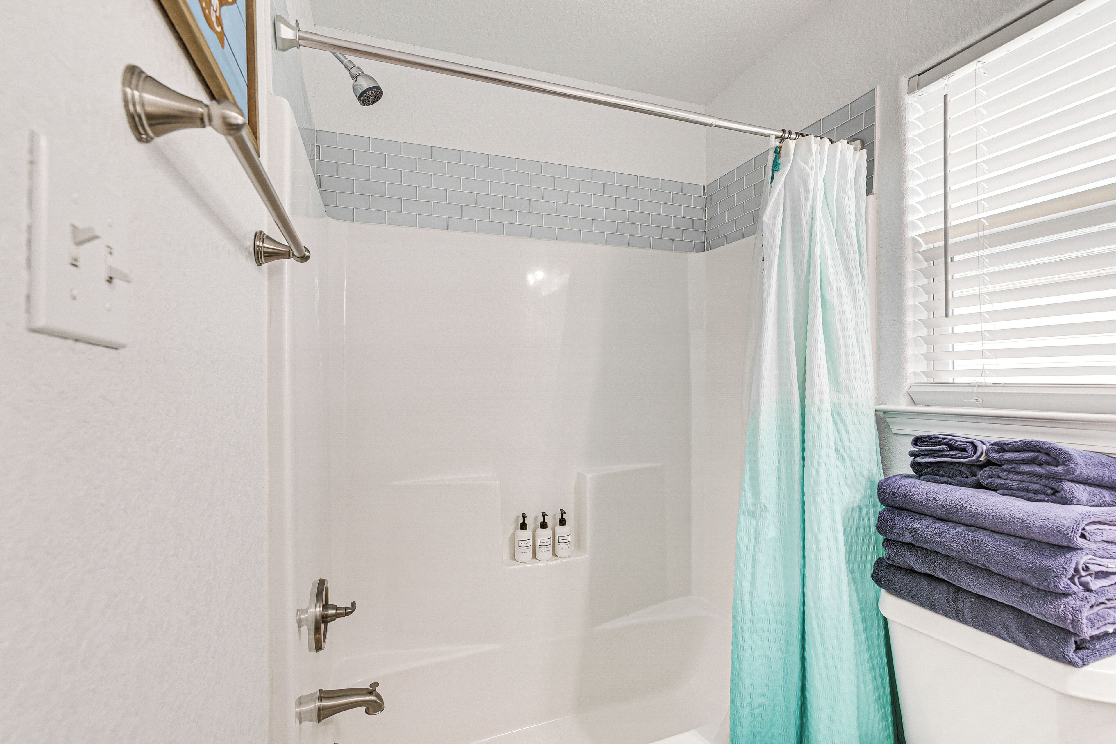 A shower area with a glass door, a towel rack with folded towels, and a window with blinds.