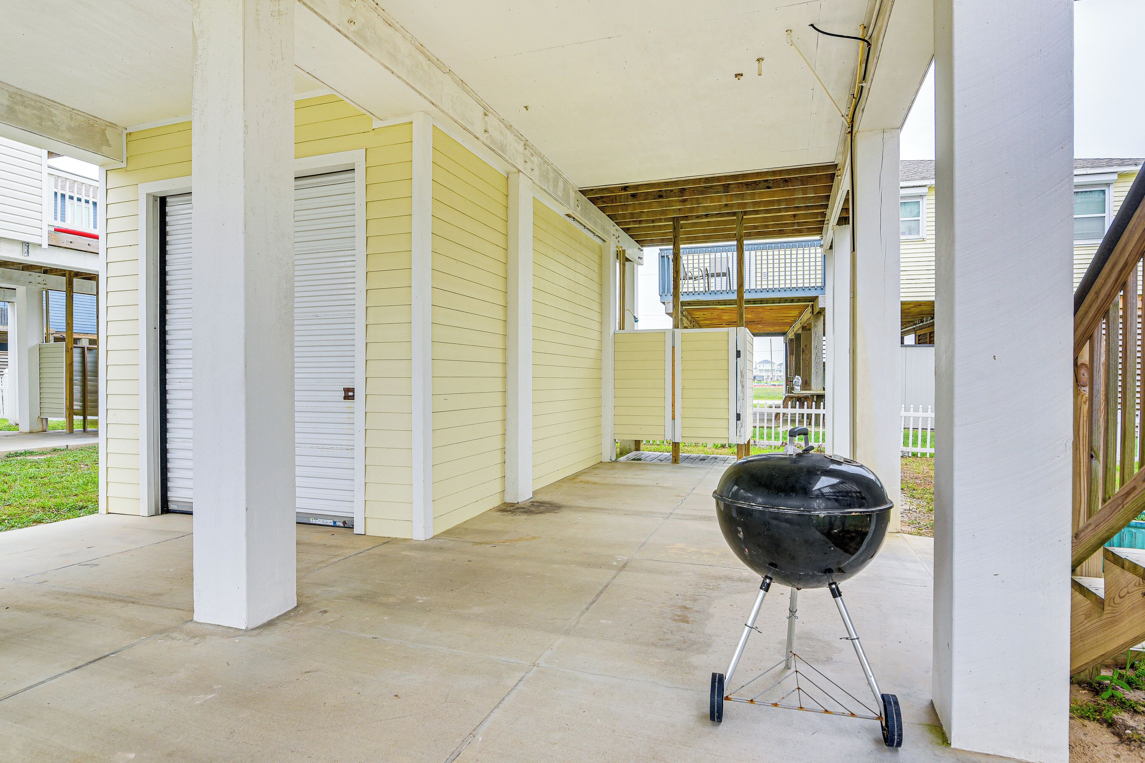 A covered patio area with a barbecue grill, concrete flooring, and a view of neighboring houses.