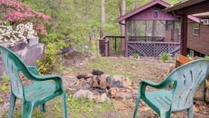 Une cabane dotée d’une terrasse, entourée d’arbres et comprenant un foyer extérieur.