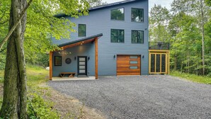 Una moderna casa a due piani con vialetto sterrato, terrazza in legno e garage.