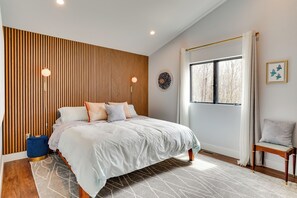 A modern bedroom with a bed, wooden panel wall, window, and a small table. - Swanton Retreat w/ Game Room, Hot Tub & Trails! (Swanton)
