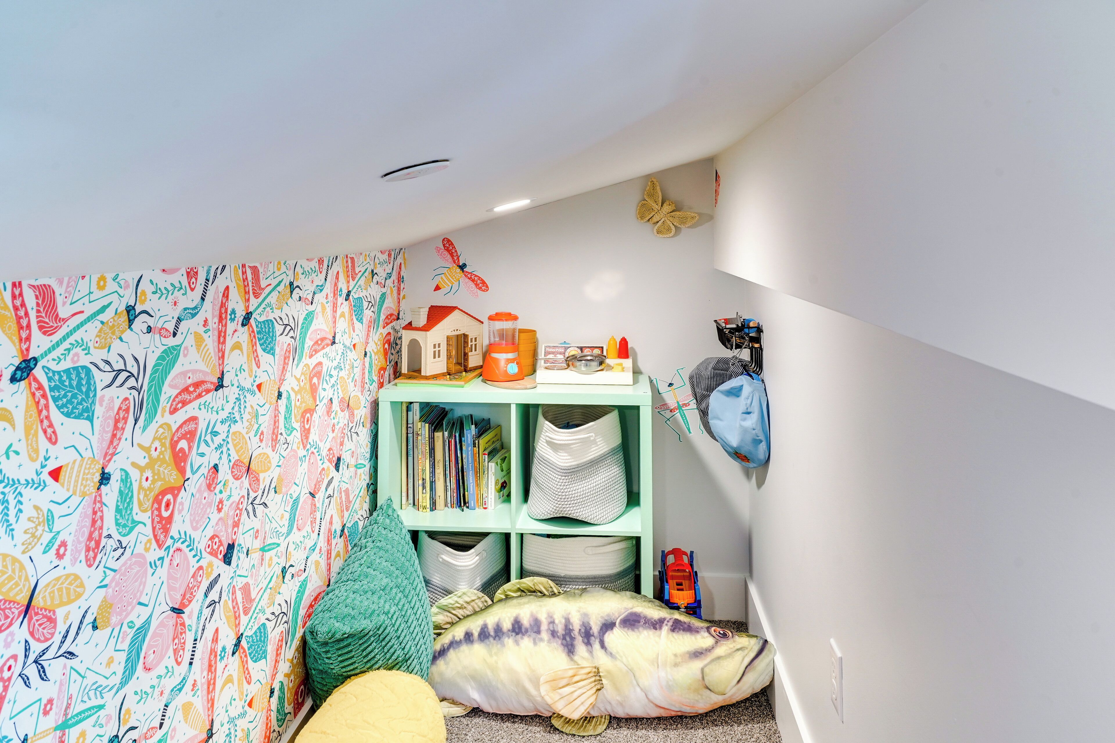 A cozy room with a colorful fish-themed wall, a bookshelf with various items, and a green storage unit.