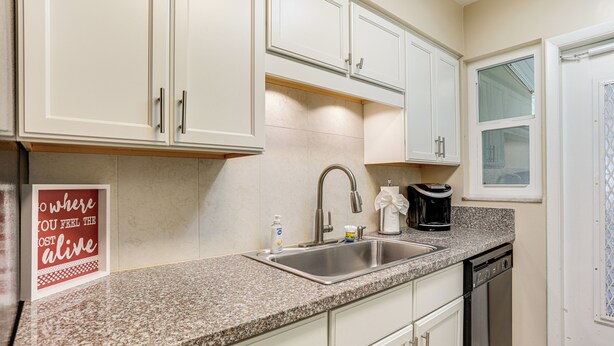 A kitchen with white cabinets, a granite countertop, a stainless steel sink, a coffee maker, and a dishwasher.