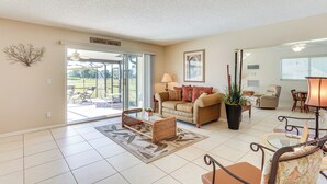 A spacious living room with a sofa, coffee table, and chairs. There is a sliding glass door leading to an outdoor patio area.