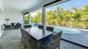 Ein Poolbereich mit Tisch und Stühlen, großen Fenstern und Blick auf den Pool und die Grünanlage.