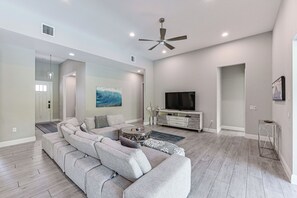 A modern living room with a sectional sofa, a ceiling fan, recessed lighting, a flat-screen TV, and a painting on the wall. - Marco Island Home w/ Pool & Hot Tub Near Beaches! (Marco Island)