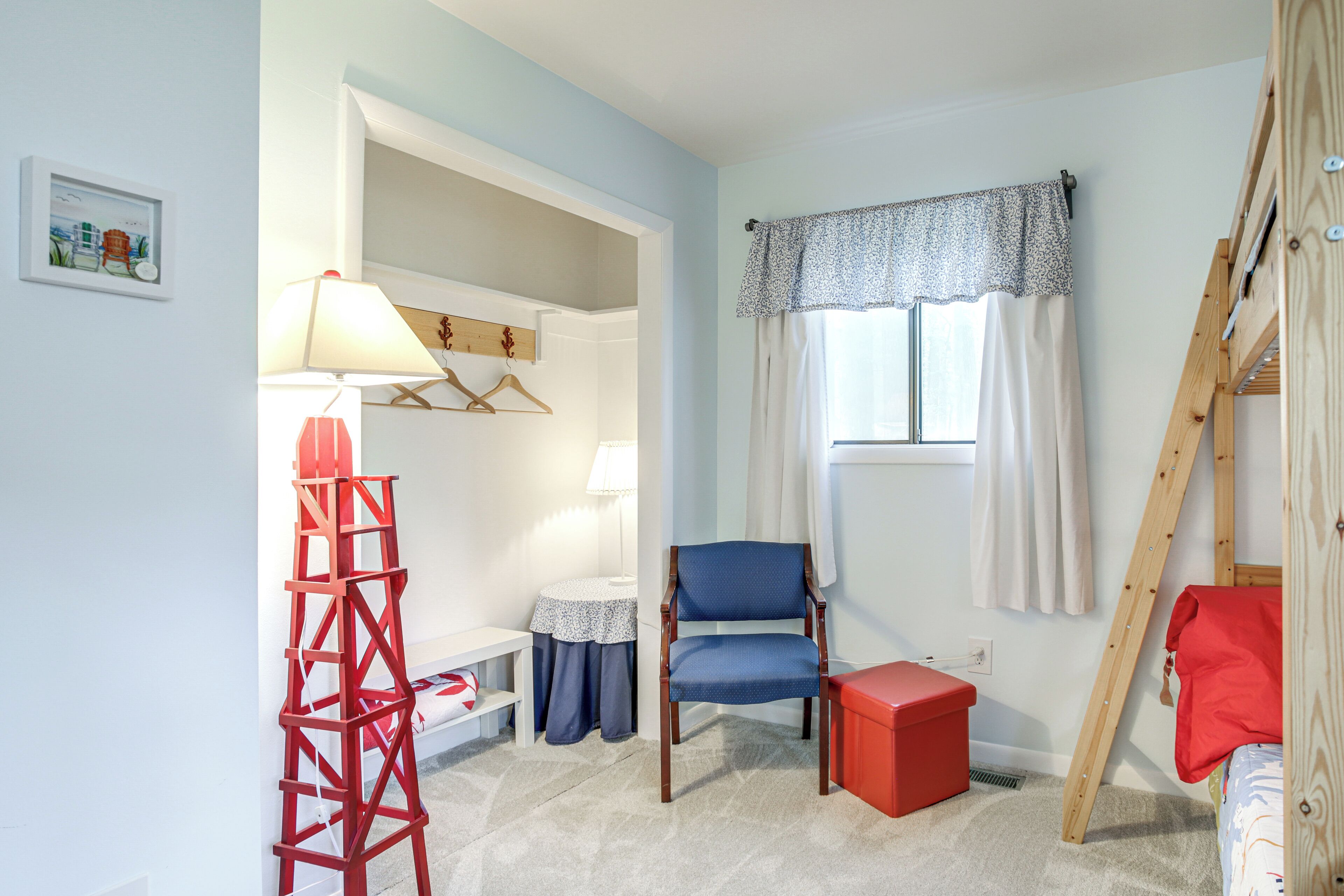 A room with a blue chair, a red storage box, a wooden ladder, a lamp, and a window with curtains.
