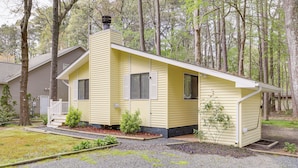 Une petite maison jaune à un seul étage, dotée d’une cheminée et entourée d’arbres.