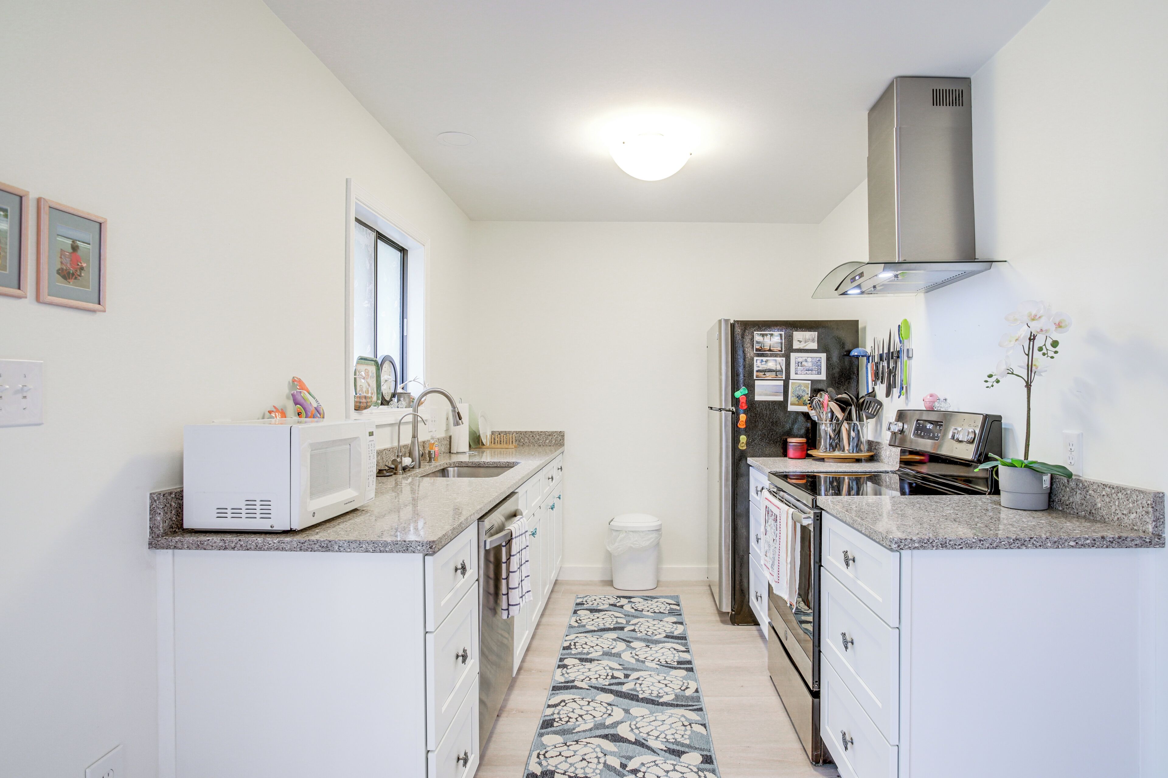 A compact kitchen with white cabinetry, a microwave, a sink, and a stainless steel range hood.