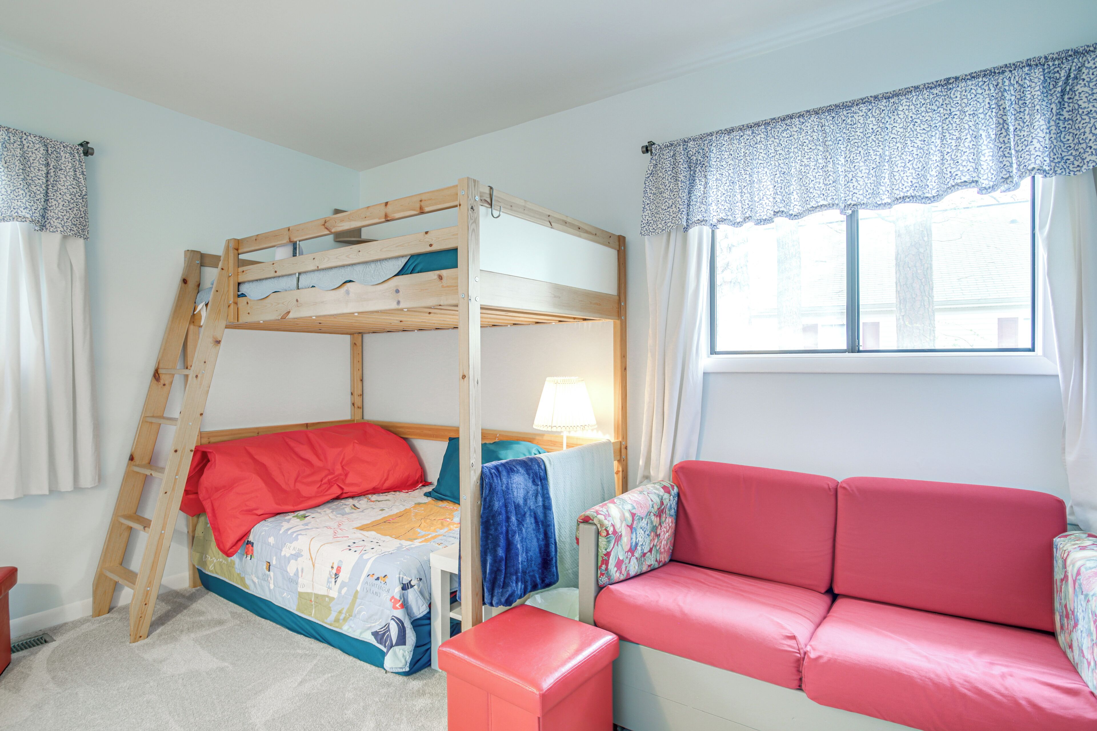 A bunk bed with a ladder, a red sofa, and a window with curtains.