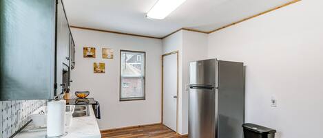Una cocina compacta con refrigerador de acero inoxidable, piso de madera y encimera blanca.