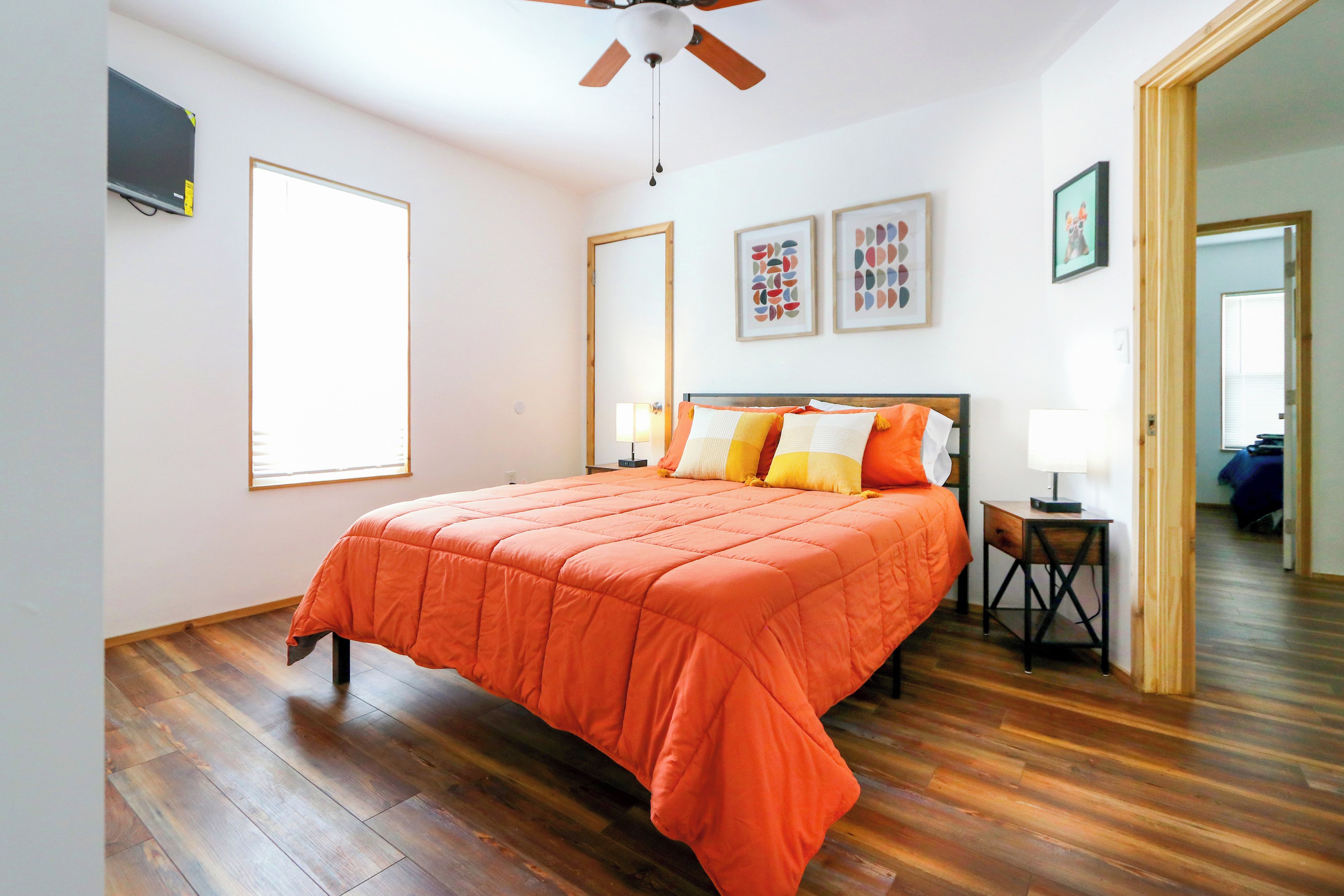 Un dormitorio con una cama grande, piso de madera, ventilador de techo y una ventana.
