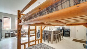 A loft-style bedroom with a wooden ladder, a plaid bedspread, and a kitchen area with bar stools and a stove. - Riverfront Briceville Apt: Atv, Hike & More! (Briceville)