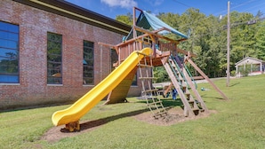 A playground with a yellow slide and a wooden climbing structure, set against a brick building with large windows. - On-site Hiking & ATV Trails: Briceville Studio (Briceville)