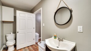 Une salle de bain comprenant des toilettes, un lavabo, un miroir et une porte donnant sur une autre pièce.