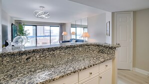 A modern kitchen with granite countertops, a large window, and a city view. - Ocean-view Balcony: Peaceful Forest Dunes Condo! (Myrtle Beach)