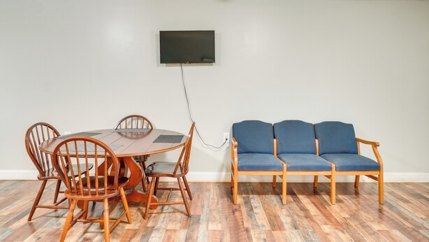 A dining area with a wooden table and chairs, a blue sofa, and a mounted TV. - ATV Trails & Adventure: Briceville Mountain Studio (Briceville)