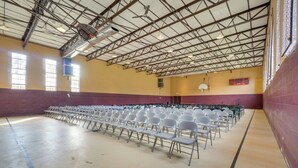 A large indoor space with rows of white folding chairs, a high ceiling with metal beams, and windows allowing natural light. - ATV Trails & Adventure: Briceville Mountain Studio (Briceville)