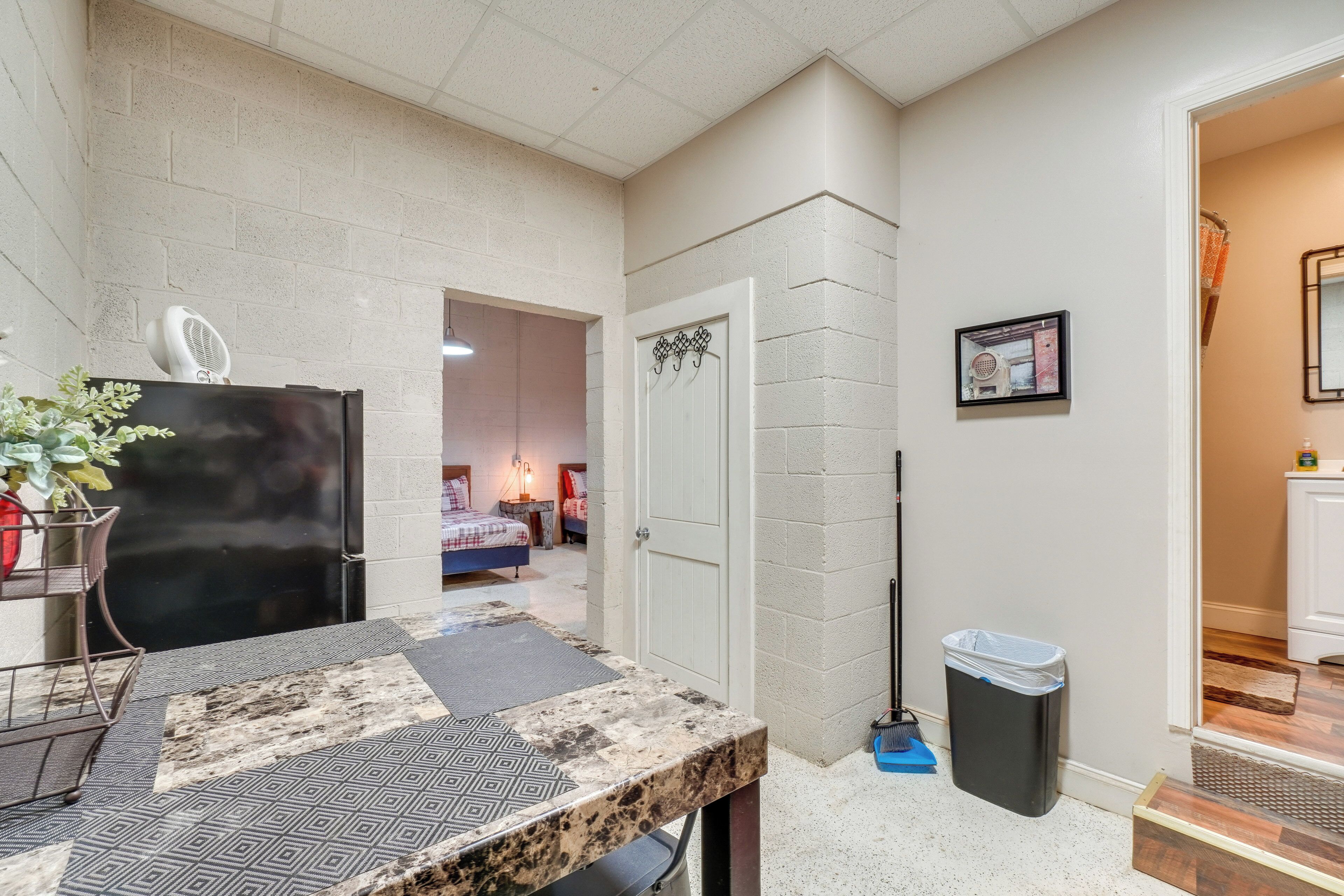 A compact living space with a kitchenette, a door leading to another room, a trash bin, and a broom.
