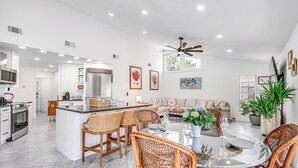 Una cocina moderna con armarios blancos, electrodomésticos de acero inoxidable y una zona de comedor con sillas de mimbre y una mesa de vidrio.