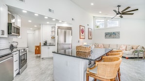 Una cocina moderna con una isla central, electrodomésticos de acero inoxidable y un comedor con sillas de mimbre.