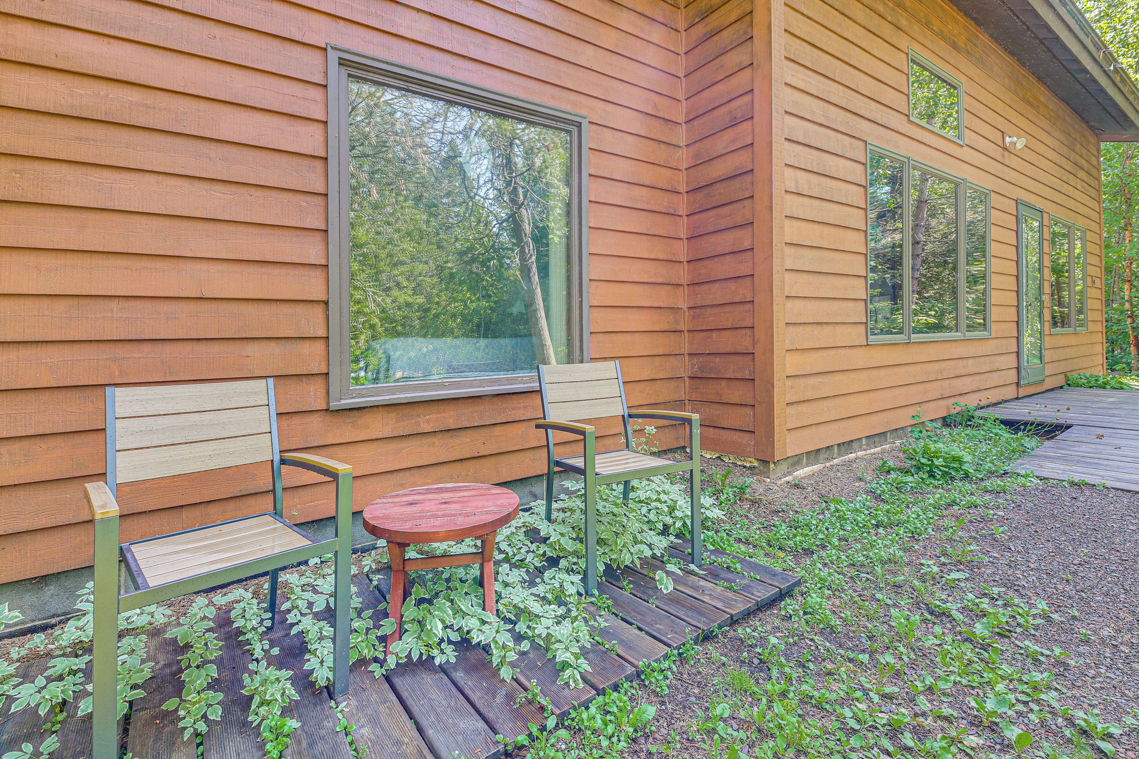Une cabane en bois avec une grande fenêtre, deux chaises et une petite table à l’extérieur.