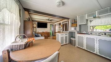 A compact kitchen with a dining area, a ceiling fan, and a television mounted on the wall.