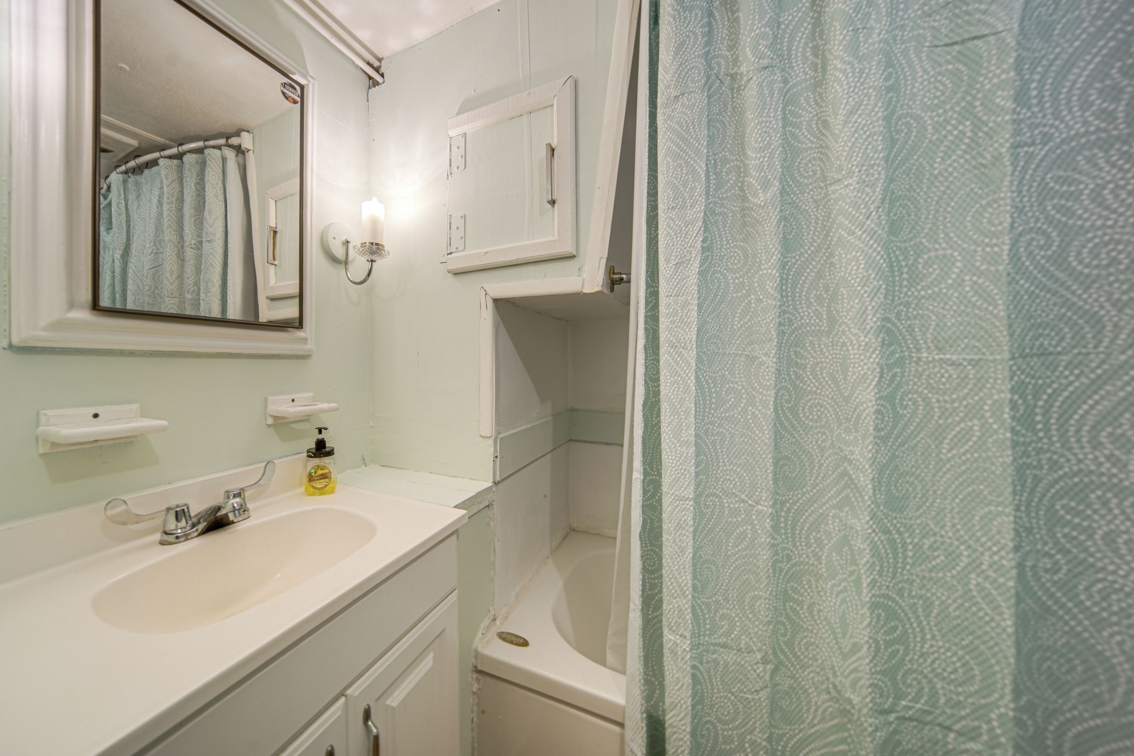 A bathroom with a white sink, a mirror, a towel rack, and a shower curtain.
