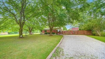 A gravel driveway leading to a house with a red fence and a grassy yard.